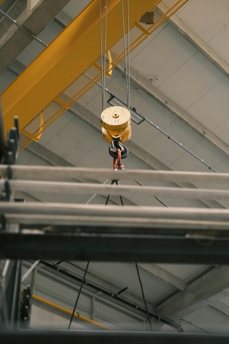 Close-up of an industrial crane hook lifting metal beams in a warehouse.