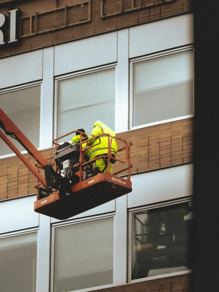 Two workers on a cherry picker doing maintenance on a building façade.